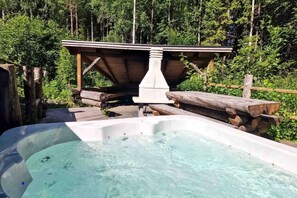A hot tub with a wooden deck and a stone structure in a forested area.