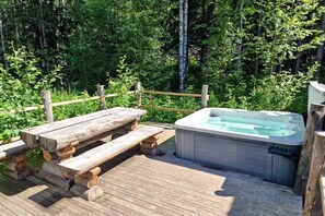 A wooden deck with a hot tub and picnic table surrounded by lush greenery.