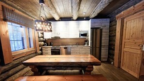 A rustic wooden interior with a large wooden table and bench, a kitchen with modern appliances, and a log wall.