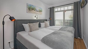 Ein Schlafzimmer mit Bett, Nachttisch, Wand-Fernseher und einem Fenster mit Vorhängen.