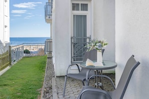 A balcony with a table and chairs, a small garden, and a view of the sea.