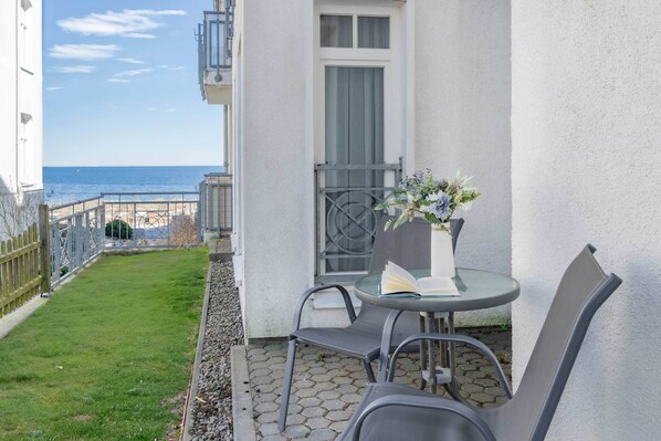 Ein Balkon mit Tisch und Stühlen, ein kleiner Garten und Meerblick.