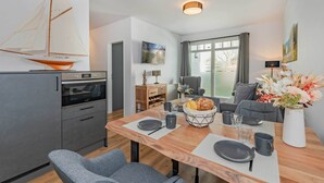 Eine moderne Küche mit einem Segelboot-Modell, einem Essbereich mit Holztisch, Stühlen und einem Blumenstrauß.