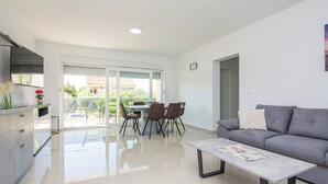 A modern living room with a grey sofa, a coffee table, and a dining area with chairs and a table. - Apartments Grabovickic (Vir)