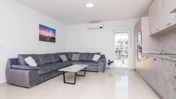 A modern living room with a grey sectional sofa, a coffee table, and a painting of a sunset on the wall. - Apartments Grabovickic (Vir)