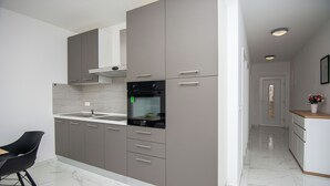 A modern kitchen with grey cabinets, a black oven, and a marble countertop. - Apartments Grabovickic (Vir)