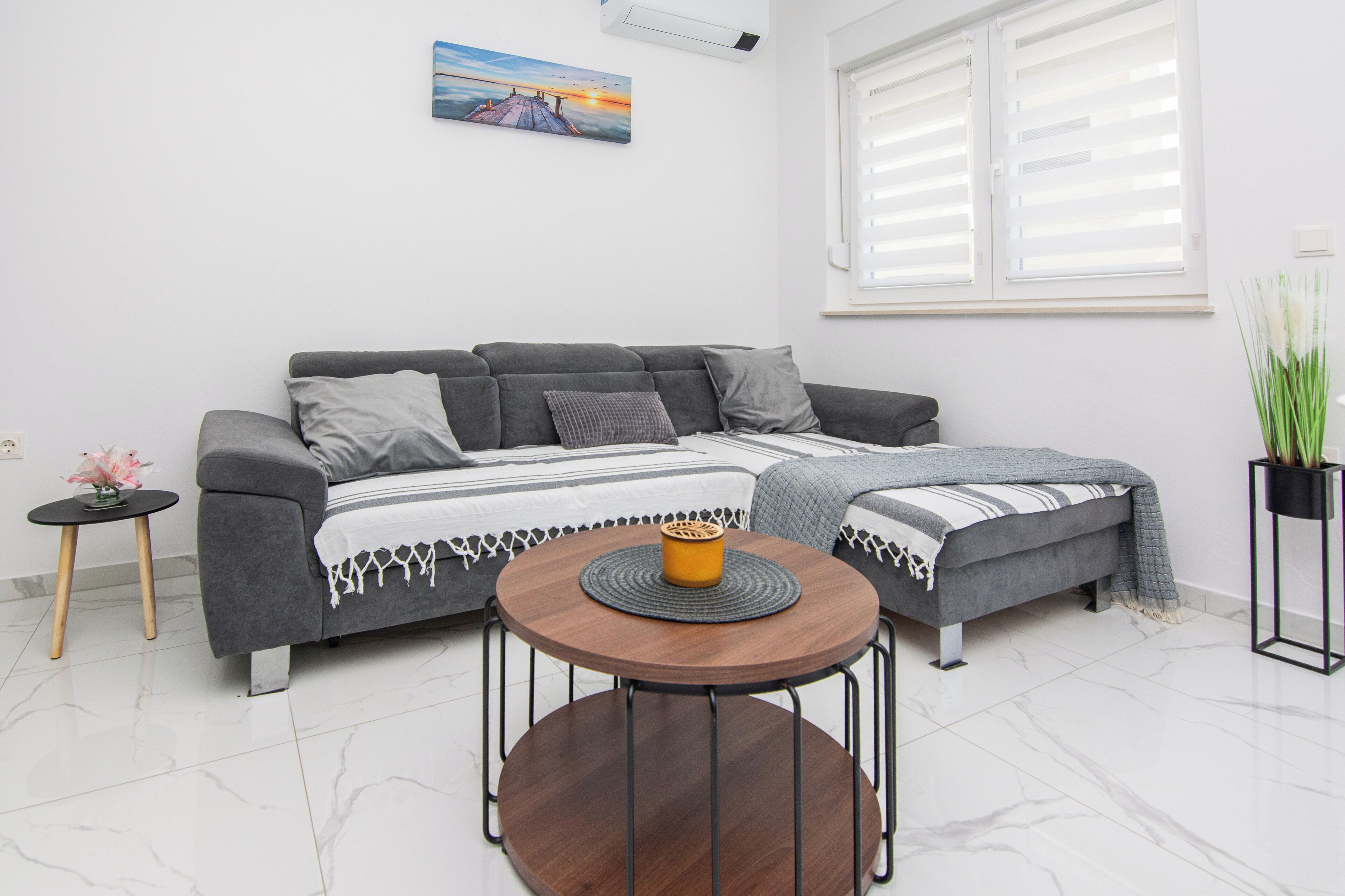 Una sala de estar moderna con un sofá seccional gris, una mesa de centro redonda de madera y una planta en maceta.