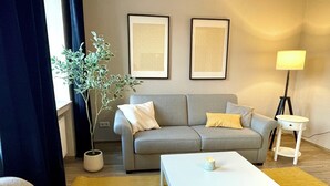 Ein Wohnzimmer mit grauem Sofa, weißem Couchtisch, einer Topfpflanze und zwei gerahmten Bildern an der Wand.