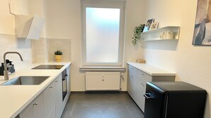 Eine moderne Küche mit weißen Schränken, einem schwarzen Kühlschrank, einem Fenster mit satiniertem Glas und einem Topf mit Pflanze auf der Arbeitsfläche.