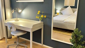 Ein Hotelzimmer mit weißem Schreibtisch, einem Stuhl, einem kleinen Topfpflanzen und einem Bett mit weißer Bettwäsche.