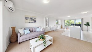 A modern living room with a sofa, a coffee table, and a dining area with a kitchen counter. - Cute & Cosy with Great Location (Moreton Bay City)