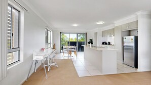 A modern kitchen with white cabinetry, a stainless steel refrigerator, and a dining area with white chairs and a table. - Cute & Cosy with Great Location (Moreton Bay City)