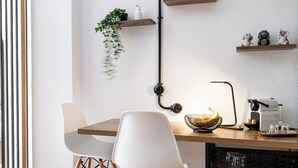 A modern kitchen with a wooden table, two white chairs, a hanging plant, and a coffee machine.