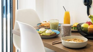 A dining area with a wooden table, a white chair, a hanging plant, and various food items.