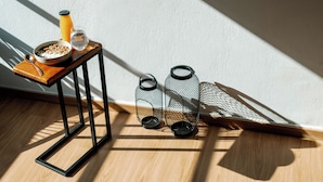 A wooden table with a bowl of cereal, a glass of water, and a spoon. There are two black wire lanterns on the floor next to the table.