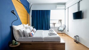 A modern hotel room with a bed, a chair, a TV, and a window with curtains.