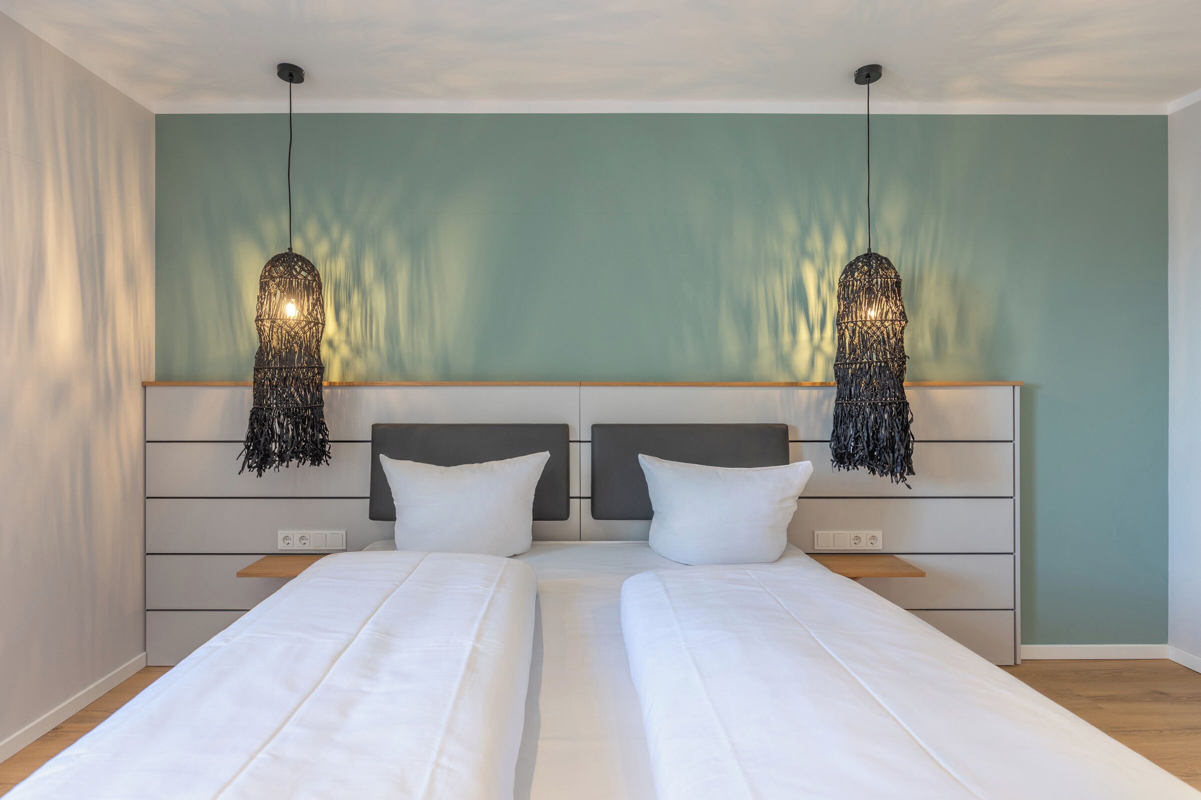 Una cama doble con sábanas blancas, cabecera de madera y dos lámparas colgantes.