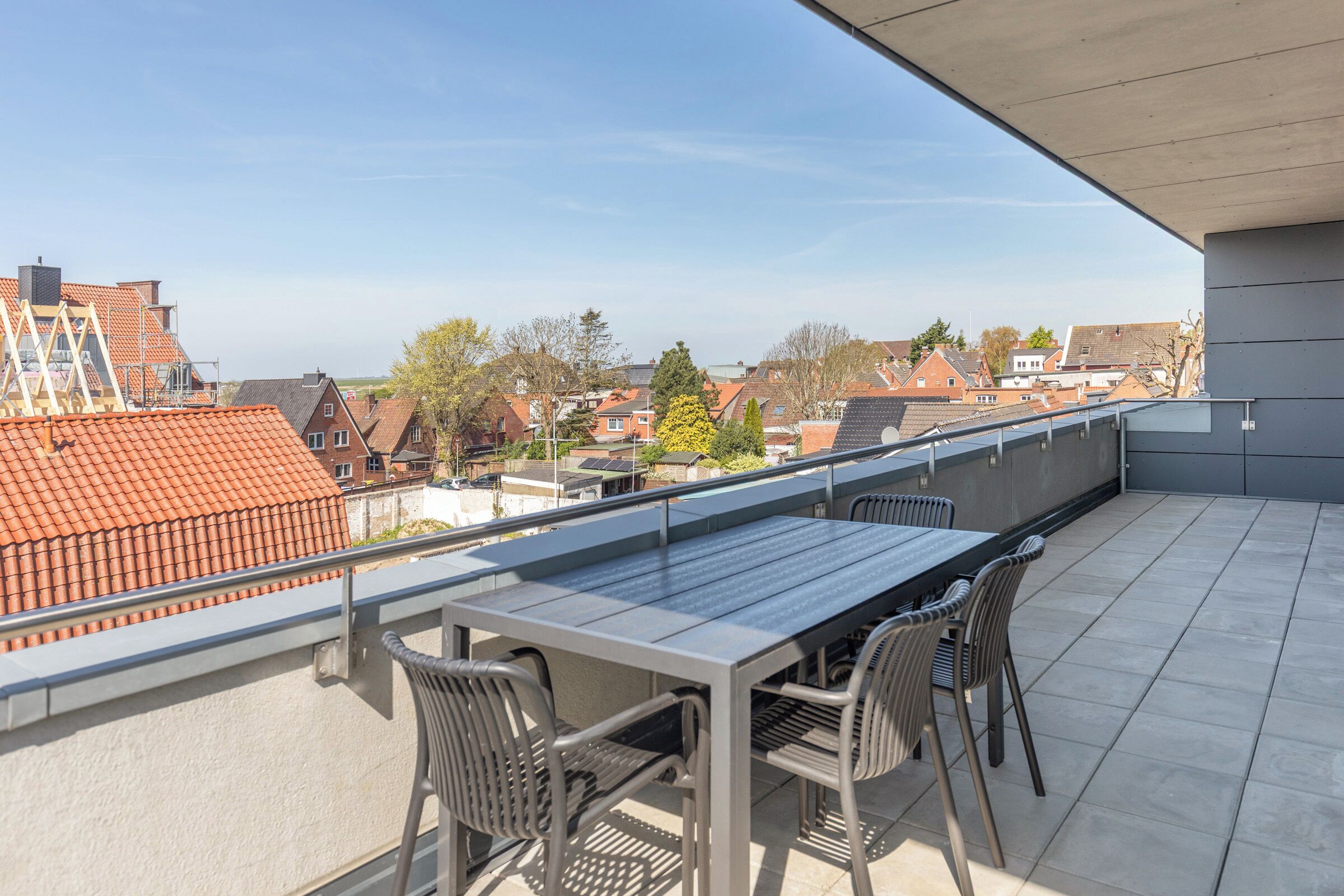 A balcony with a table and chairs, offering a view of the neighborhood.