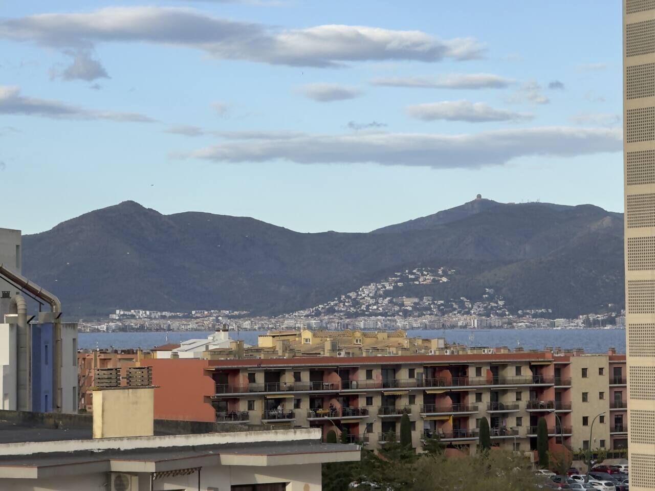 Eine Küstenstadt mit Bergen im Hintergrund, mit mehrstöckigen Gebäuden, Balkonen und Blick auf das Meer.