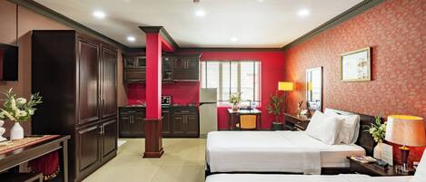 Habitación de hotel con dos camas, un escritorio, una silla, una pequeña cocina y una pared de acento roja.