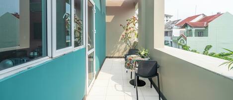 Un balcon avec une table et des chaises, un pot de fleurs et une vue sur les bâtiments voisins.