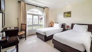 A hotel room with two beds, a desk, a chair, a window with curtains, a lamp, and a painting on the wall. - La Bonita Hotel & Apartments (Ho Chi Minh City)