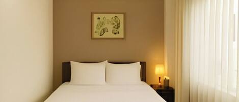 A modern hotel room with a large bed, a nightstand with a lamp, and a window with curtains.