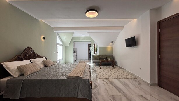 A modern bedroom with a large bed, a TV mounted on the wall, and a view into another room. - Heavens Balcony Meteora (Kalabaka)