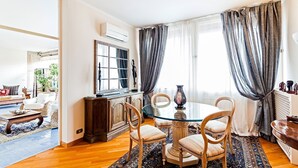 A dining area with a round glass table, wooden chairs, a cabinet, and a large window with curtains. - Casa Azul in Sorrento center - My Rental Homes (Sorrento)