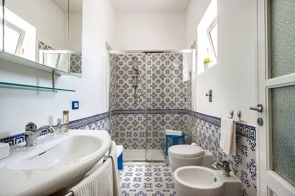 A bathroom with a white sink, a toilet, and a shower with patterned tiles.