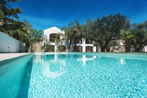 A clear swimming pool with a white building in the background, surrounded by trees.