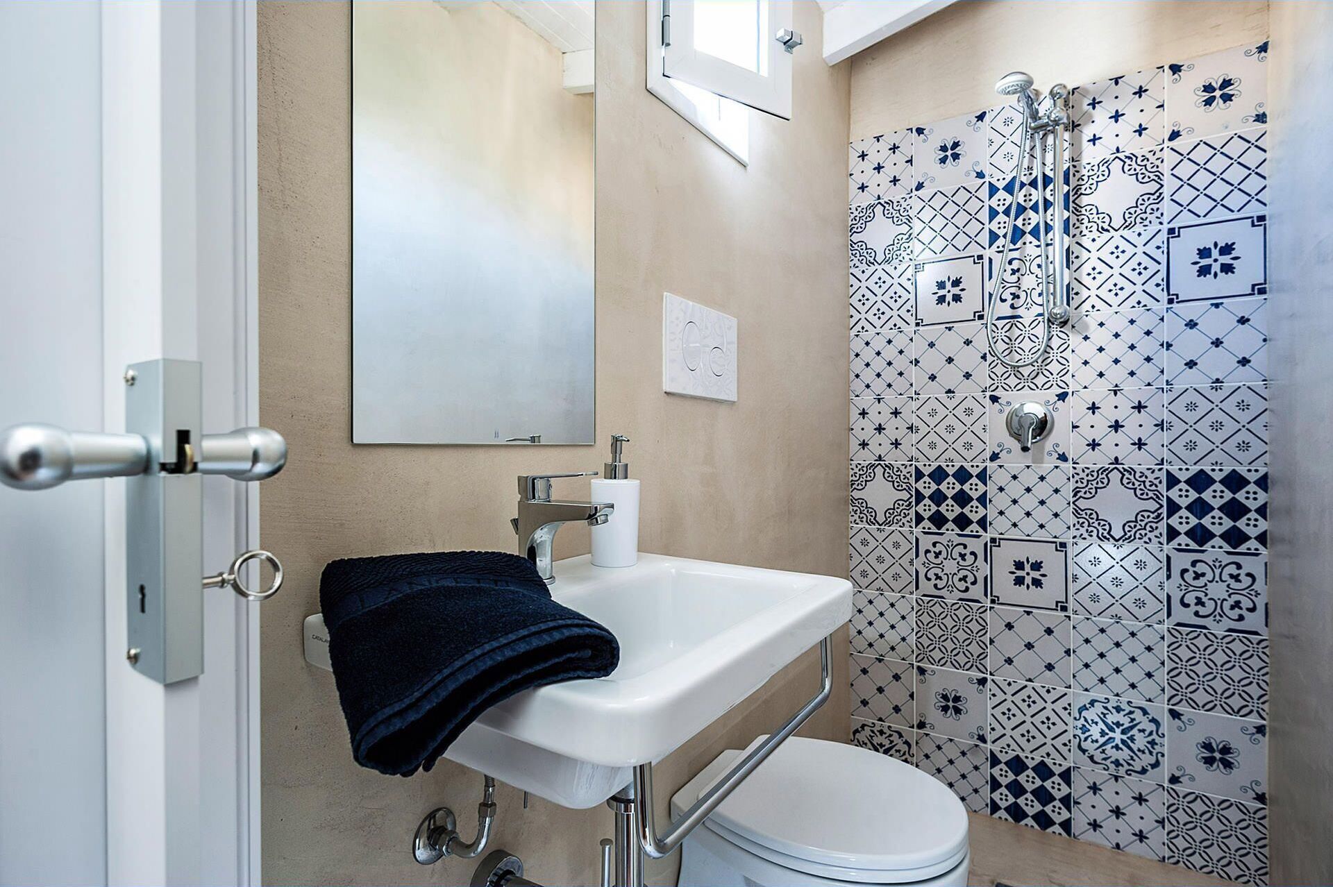 Uma casa de banho com lavatório branco, uma toalha, sanita e chuveiro com azulejos estampados.