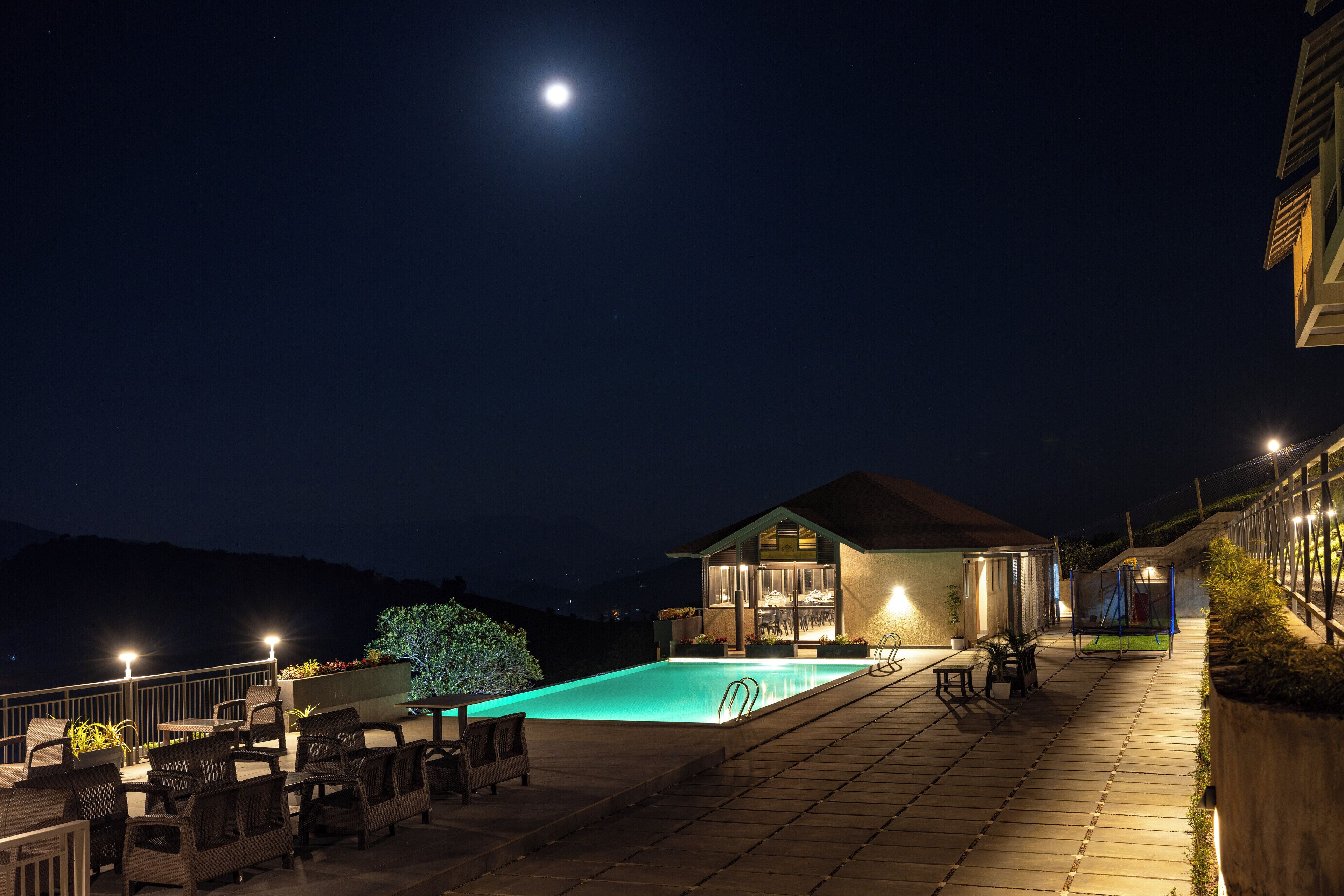 Vue nocturne d’un espace piscine avec des sièges d’extérieur et une maison.
