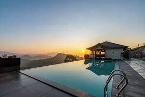 Ein Swimmingpool mit Blick auf Berge bei Sonnenuntergang, ein überdachter Sitzbereich und eine Terrasse mit einem Stuhl.