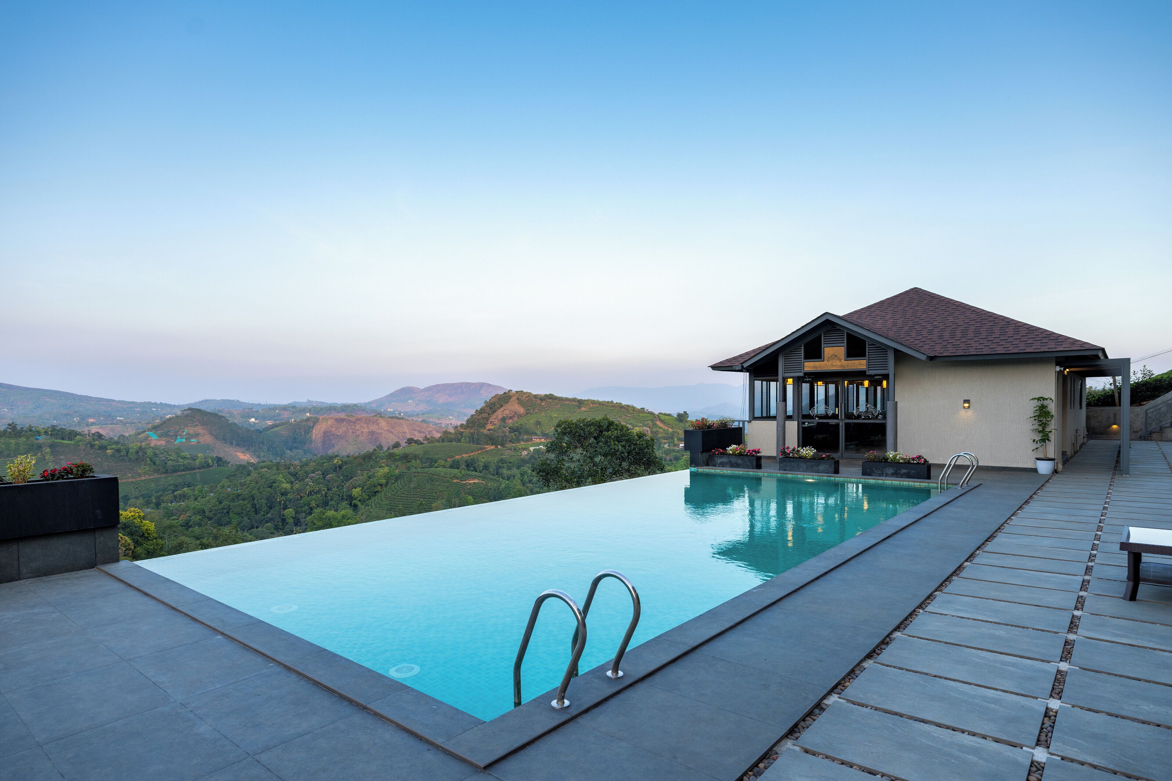 Ein moderner Infinity-Pool mit freiem Blick auf die umliegende Landschaft, ein kleines Gebäude mit Satteldach und ein Kiesweg.