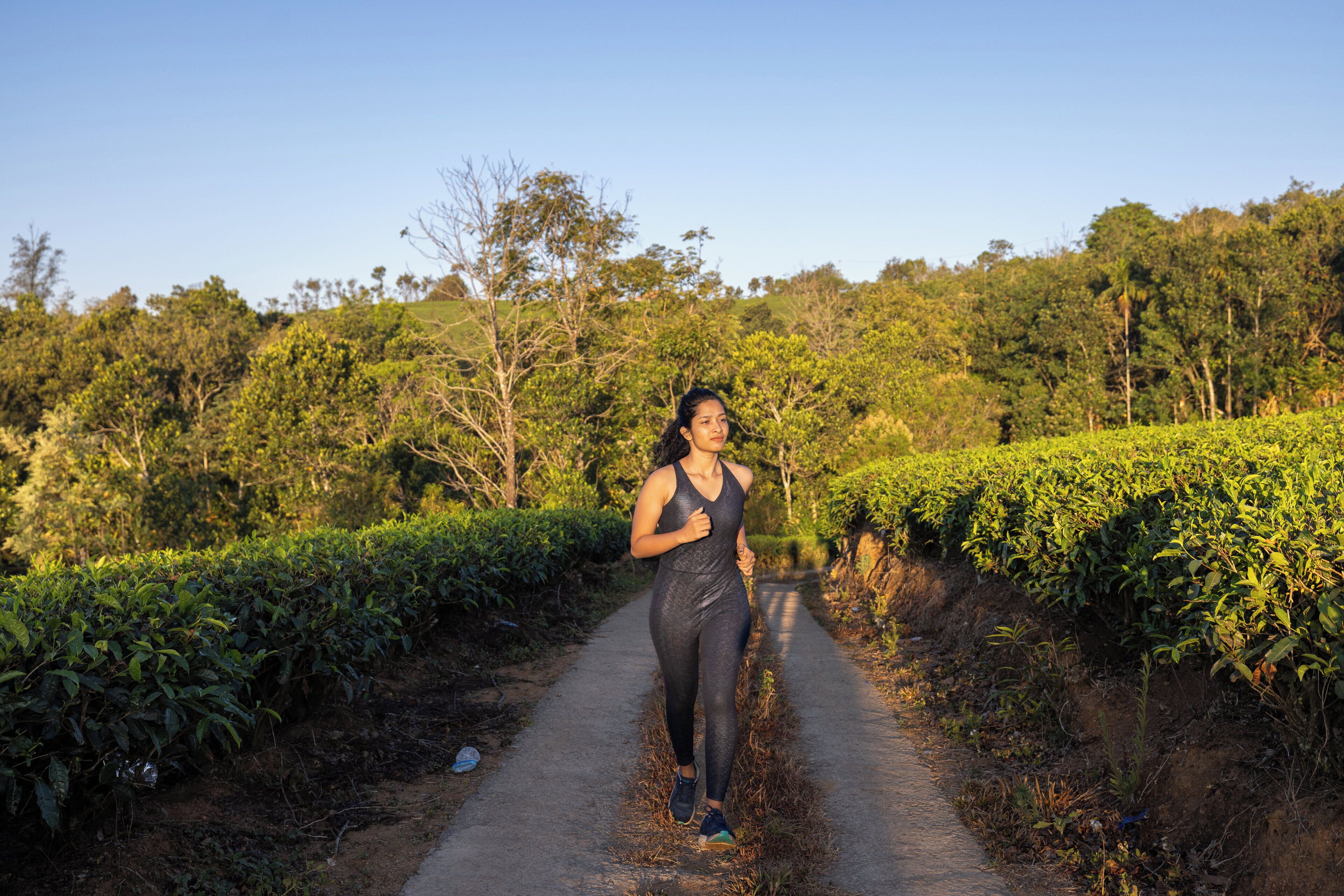 A woman jogging on a dirt path surrounded by lush greenery.