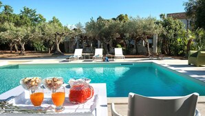 A poolside table with breakfast items and a chair facing the pool. - Green Villa with heated pool - My Rental Homes (Salemi)