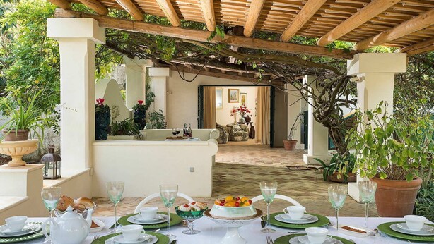 An outdoor dining area with a pergola, tables set with green plates, white teapots, and wine glasses. - Green Villa with heated pool - My Rental Homes (Salemi)