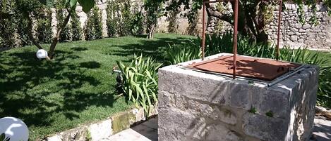 Een gebouw van steen met een metalen dak, omgeven door een goed onderhouden tuin met gras en planten.