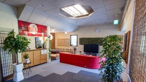 Un espace d’accueil avec un comptoir rouge, un téléviseur et des plantes en pot.
