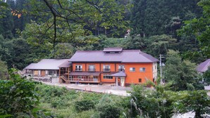 Un bâtiment à deux étages, avec un toit rouge et des murs orange, entouré d’une végétation luxuriante et d’arbres.