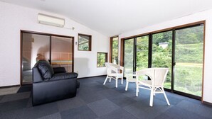 Un salon moderne avec un canapé en cuir noir, des fauteuils en osier blancs et une grande porte-fenêtre coulissante donnant sur un jardin.