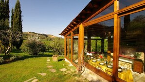 Un área de comedor al aire libre cubierta con una mesa preparada para dos personas, rodeada de paredes de vidrio.
