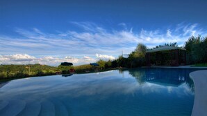 Piscina cristalina con un pabellón y sillas de descanso, rodeada de follaje y colinas.