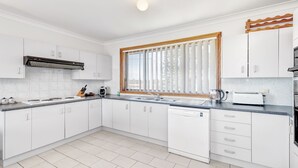 A modern kitchen with white cabinets, a built-in oven, and a window with blinds. - 2 Storey family home just steps away from the beach! (Culburra Beach)