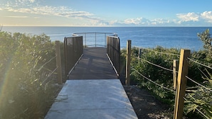 A concrete pathway leading to a metal gate with a view of the sea. - 2 Storey family home just steps away from the beach! (Culburra Beach)
