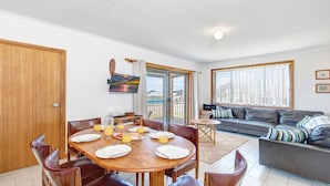 A dining area with a wooden table set for breakfast, a sofa, and a balcony with a view. - 2 Storey family home just steps away from the beach! (Culburra Beach)