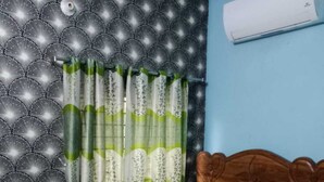 A bedroom with a patterned headboard, a bed with a geometric patterned bedspread, green curtains, and a wooden headboard. - Hotel New Royal Jatrabari (Dhaka)