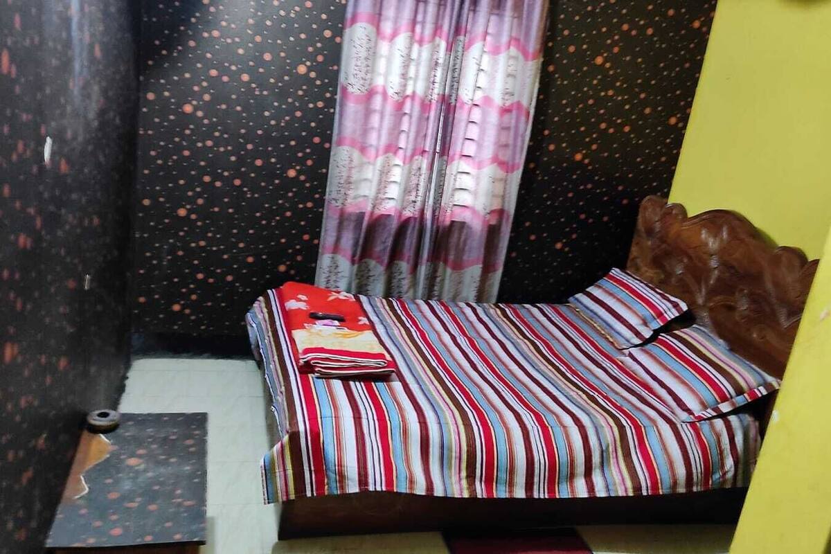 Une petite pièce, de taille modeste, comprenant un lit simple, un oreiller, une petite table et un rideau.