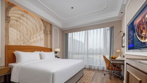Habitación de hotel con una cama grande, un escritorio, una silla, un televisor y vistas a la ciudad por la ventana.